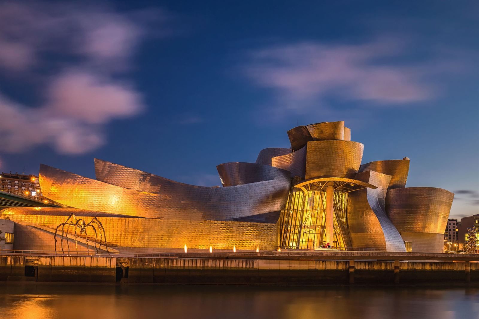 The curved titanium walls of the Guggenheim Museum Bilbao glowing at dusk beside the river