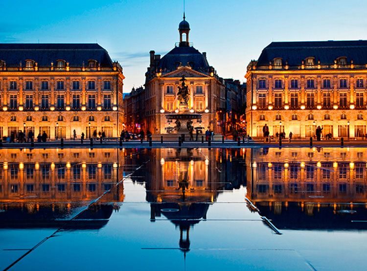 The Place de la Bourse in Bordeaux lit at dusk and reflected in the shallow Miroir d&rsquo;Eau