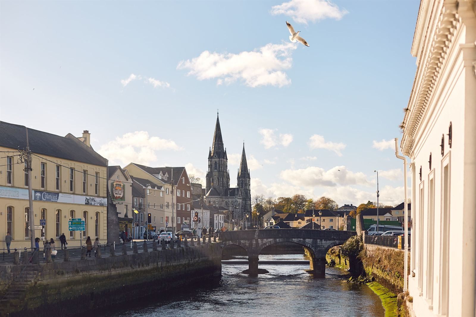River Lee and a stone arched bridge in Cork, with the triple spires of a Gothic cathedral behind