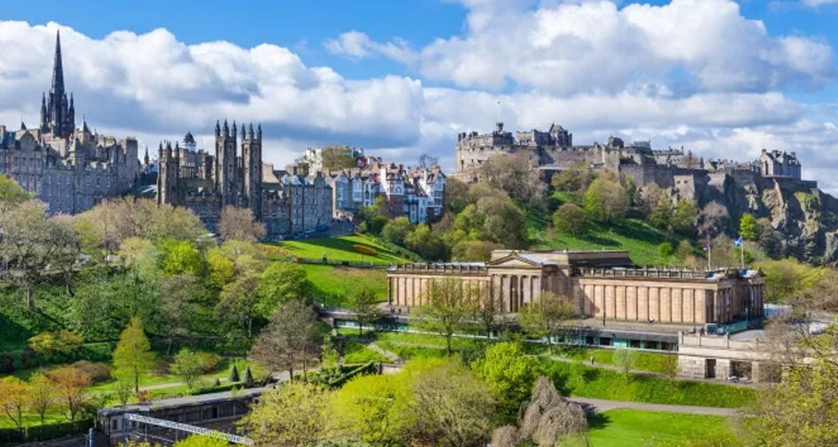 Edinburgh Castle on its rock above the green slopes of Princes Street Gardens, with Gothic spires and a columned gallery building in the gardens below