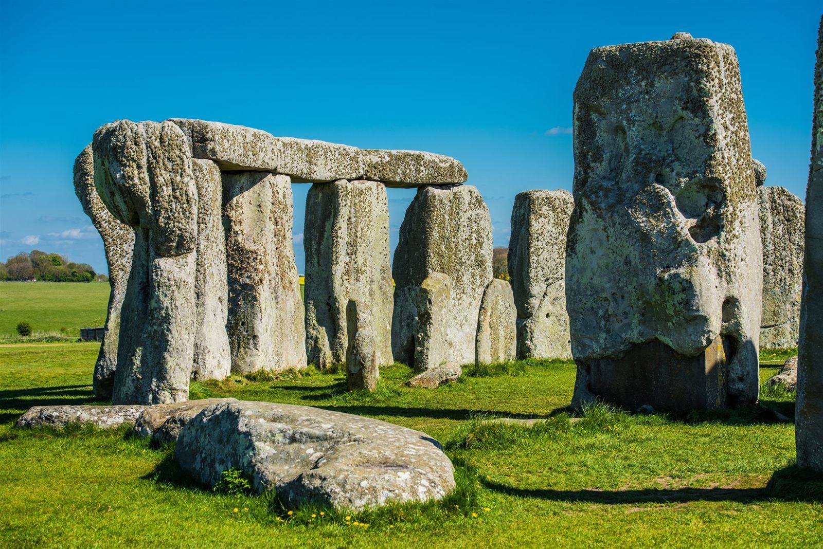 The standing stones and lintels of Stonehenge on green grass under a clear blue sky
